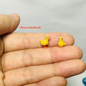 May include: Two small crocheted yellow ducklings with orange beaks and feet. The ducklings are sitting on a person's hand.