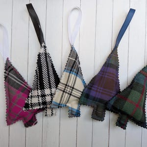 Può includere: Cinque decorazioni in tessuto a forma di albero di Natale, ognuna con un motivo a quadri distinto in colori che includono rosa, nero, bianco, blu, viola e verde. Ogni decorazione è dotata di un nastro sulla parte superiore per appenderla.