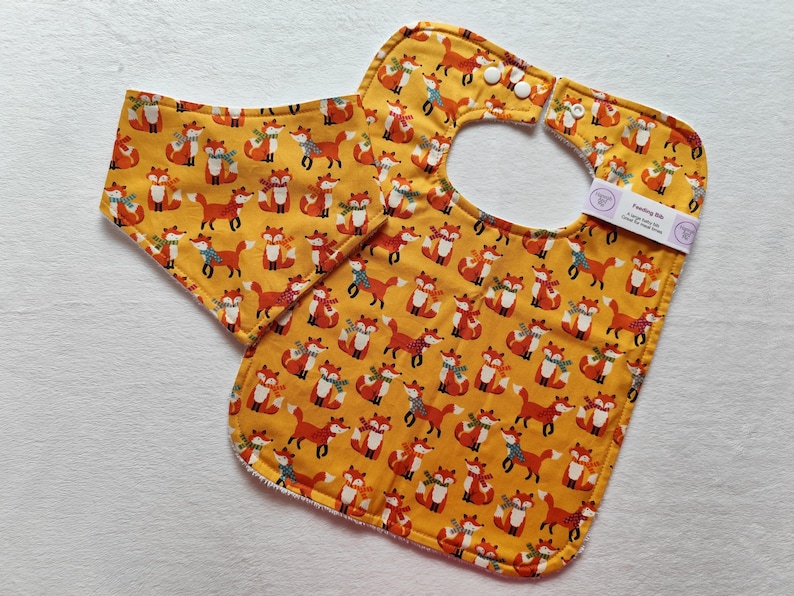 May include: A yellow bib with a fox print and a matching burp cloth. The bib has a snap closure and the text "Sewing Bib" is printed on the cloth.