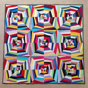 May include: A vibrant, geometric quilt with a repeating pattern of squares. Each square features a colourful array of colours, including red, blue, green, yellow, and purple. The quilt is bordered with a dark grey fabric.