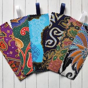 May include: Five fabric bookmarks with vibrant batik patterns. Each bookmark features a unique design, including floral and geometric motifs, in shades of purple, green, blue, and orange. White or navy blue ribbon loops are attached at the top.