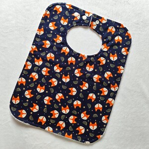 May include: A blue baby bib with a white trim and a pattern of orange fox faces on a dark blue background.