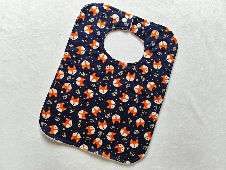 May include: A blue baby bib with a white trim and a pattern of orange fox faces on a dark blue background.