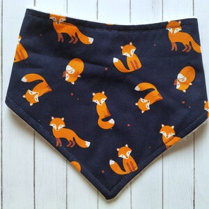 May include: A black bandana with a white trim features a repeating pattern of orange foxes. The foxes are in various poses, including walking, sitting, and looking up.