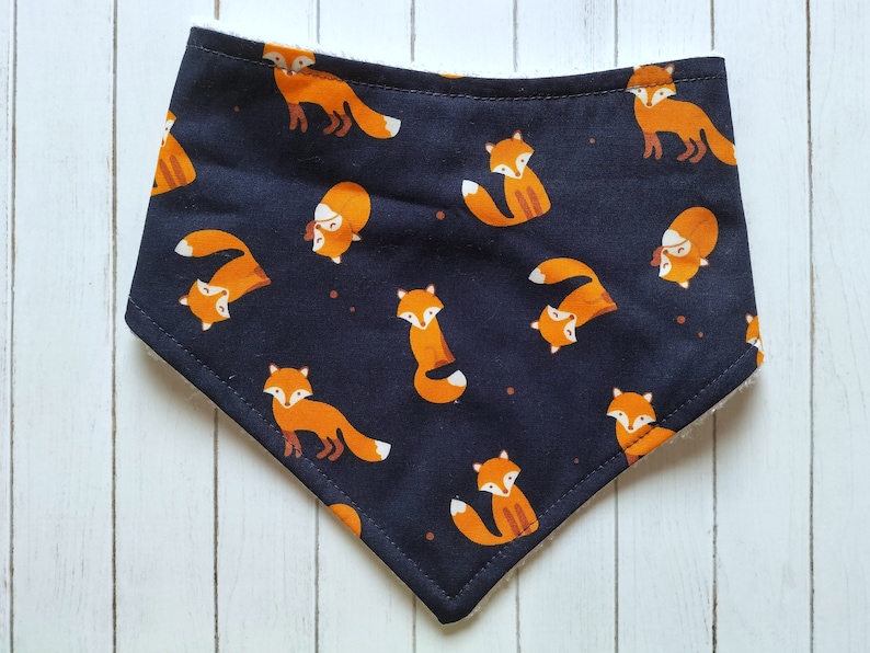 May include: A black bandana with a white trim features a repeating pattern of orange foxes. The foxes are in various poses, including walking, sitting, and looking up.