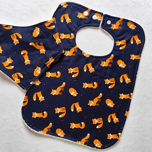 May include: A blue and white baby bib with a fox print. The bib has a white fleece lining and a snap closure.