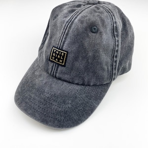 Könnte beinhalten: Eine schwarze, abgenutzte Baseballkappe aus Baumwolle mit einem goldenen quadratischen Aufnäher, auf dem "THIS GIRL CAN" steht.