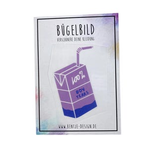 Könnte beinhalten: Ein Bügelbild in Lila und Blau mit einem Saftkarton-Design und einem Strohhalm. Auf dem Saftkarton steht der Text "100% BOY TEARS". Die Wörter "BÜGELBILD" und "VERSCHÖNERE DEINE KLEIDUNG" sind oben aufgedruckt.