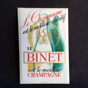 Cartel publicitario vintage de metal sobre cartón con el texto “LE BINET” de Champagne. Puede colgarse o colocarse de pie.