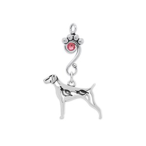 May include: A silver-toned pendant featuring a dog silhouette with intricate detailing. The pendant is connected to a paw print charm with a pink gemstone center. The design is elegant and suitable for dog lovers.