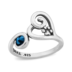 Può includere: Anello in argento sterling con una pietra preziosa blu e un design a forma di cuore con un dettaglio a forma di zampa. L'anello è timbrato "D.R.P.J. .925".