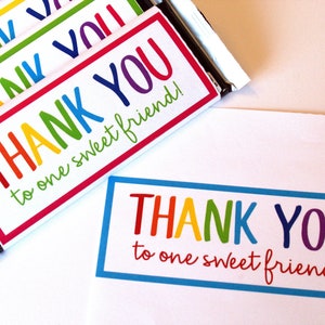 May include: A set of rainbow-colored chocolate bar wrappers with the text "THANK YOU to one sweet friend!" printed on them.