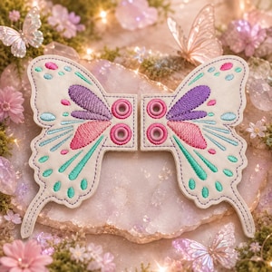 Op de afbeelding: Twee geborduurde vlindervleugelpatches. De vleugels zijn gebroken wit met paarse, roze en turquoise accenten. Elke vleugel heeft een reeks roze cirkels in het midden. De patches zijn ontworpen met een gestikte omtrek en zijn waarschijnlijk bedoeld voor knutselen of versieren.