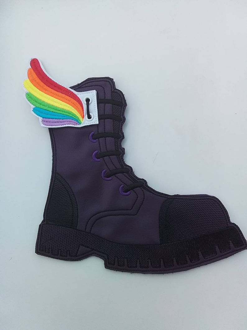 May include: A purple boot patch with a rainbow wing attached. The boot has black laces and a black sole. The wing is made of colorful threads in a rainbow pattern.