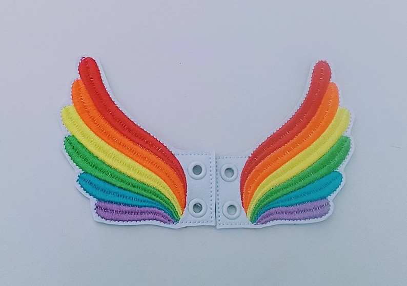 May include: Embroidered rainbow wing patches with a white backing. The wings feature a vibrant spectrum of colors, including red, orange, yellow, green, blue, and purple. Each wing has a white base with snap closures.