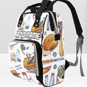 May include: A white and black diaper bag with a colorful pattern of tools and construction equipment. The bag has a large pocket on the front with the text "ADD NAME" in black.