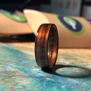 May include: A dark brown wooden ring with a polished finish. The ring has a natural wood grain pattern and is made of a single piece of wood.
