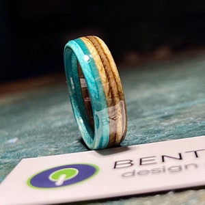 May include: A turquoise, brown, and white wooden ring with a glossy finish. The ring is made of wood and resin.