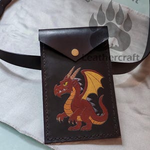 May include: Black leather wallet with a flap closure and a gold snap. The front features a red and yellow dragon illustration. The words "Wild Spirit Leathercraft" are visible in the background.