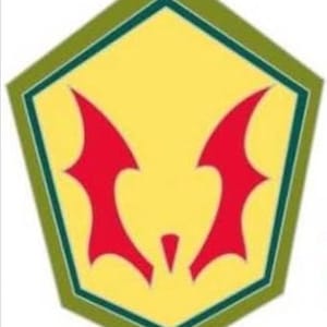 May include: A yellow pentagon-shaped emblem with a red bat-like symbol in the center. The emblem has a green border and is set against a white background. The bat symbol has two wing-like shapes.