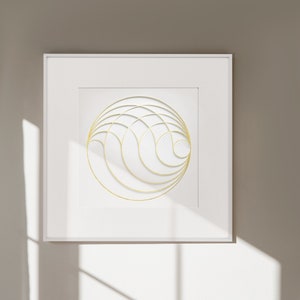 Op de afbeelding: Een witte ingelijste print met een gouden geometrisch ontwerp van overlappende cirkels en lijnen. De print hangt aan een witte muur met een witte vaas op een witte tafel ervoor.