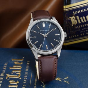 May include: A silver wristwatch with a blue face and brown leather band. The watch face has silver hands and markers, and the word "WINDSOR" is printed in the center.