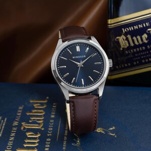 May include: A silver wristwatch with a brown leather band and a blue face. The watch face has silver hands and markers, and the word "WINDSOR" is printed in white at the top.