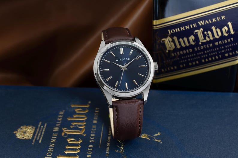 May include: A silver wristwatch with a brown leather band and a blue face. The watch face has silver hands and markers, and the word "WINDSOR" is printed in white at the top.