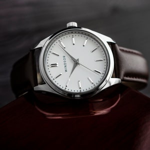 May include: A silver wristwatch with a white face and black Roman numeral hour markers. The watch has a brown leather band and says "Windsor" on the face.