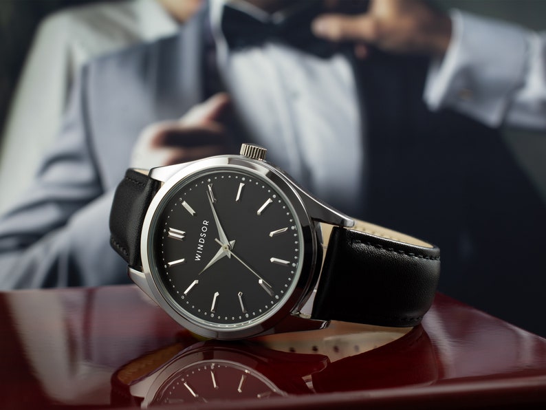 May include: A silver watch with a black leather band and a black face. The watch face has silver hands and Roman numeral hour markers. The word "WINDSOR" is printed on the face.