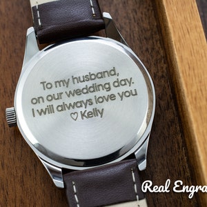 May include: A silver watch with a brown leather band. The back of the watch is engraved with the message "To my husband, on our wedding day. I will always love you ♡Kelly".
