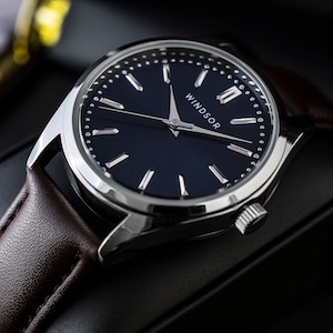 May include: A silver watch with a dark blue face and silver hands. The watch has a brown leather band and the word "WINDSOR" printed on the face.