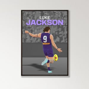 May include: A framed poster featuring a digital illustration of Australian rules football player Luke Jackson in a purple and white uniform with the number 9, kicking a yellow Sherrin football against a grey stadium crowd background.