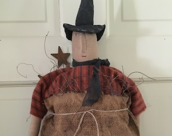 May include: A handmade Halloween witch doll with a black hat, a red and orange striped shirt, and a burlap sack body. The doll has a black scarf and a star accent. The body is tied with twine.