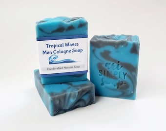 May include: Three bars of handcrafted soap with a tropical wave design. The soap is blue with gray marbling and a white label that reads "Tropical Waves Men Cologne Soap". The soap is a natural product.