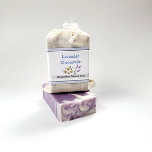 May include: A bar of lavender and chamomile soap wrapped in a natural fabric bag. The soap is a swirl of purple and white and the label reads "Lavender Chamomile Handcrafted Natural Soap".