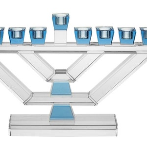 Op de afbeelding: Een heldere glazen menorah met blauwe glazen kaarshouders. De menorah heeft een modern ontwerp met een geometrische basis.