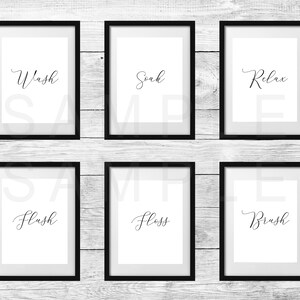 May include: Six framed bathroom art prints with black frames and white backgrounds. Each print features a cursive word: Wash, Soak, Relax, Flush, Floss, and Brush. The prints are displayed against a white-washed wooden background.