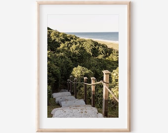 May include: A stone staircase with a rope railing leads up a grassy hill to a view of the ocean.