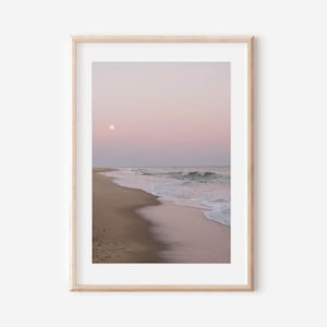 Puede incluir: Una impresión enmarcada de una escena de playa al atardecer. El cielo transita del rosa al morado, con una luna llena visible. La playa arenosa se encuentra con las olas del océano, creando un paisaje costero sereno.