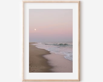 May include: A framed print of a beach scene at dusk. The sky transitions from pink to purple, with a full moon visible. The sandy beach meets the ocean waves, creating a serene coastal landscape.