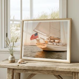 May include: A framed print of a white sailboat with an American flag, sailing on the water. The word "EXPLORER" is printed on the boat. The print is displayed on a rustic wooden table near a window.