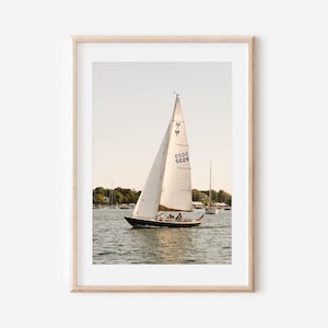 May include: A framed print of a sailboat on the water. The sailboat has a white sail with the number 5029 on it. The boat is black with a wooden deck. Other sailboats are in the background.