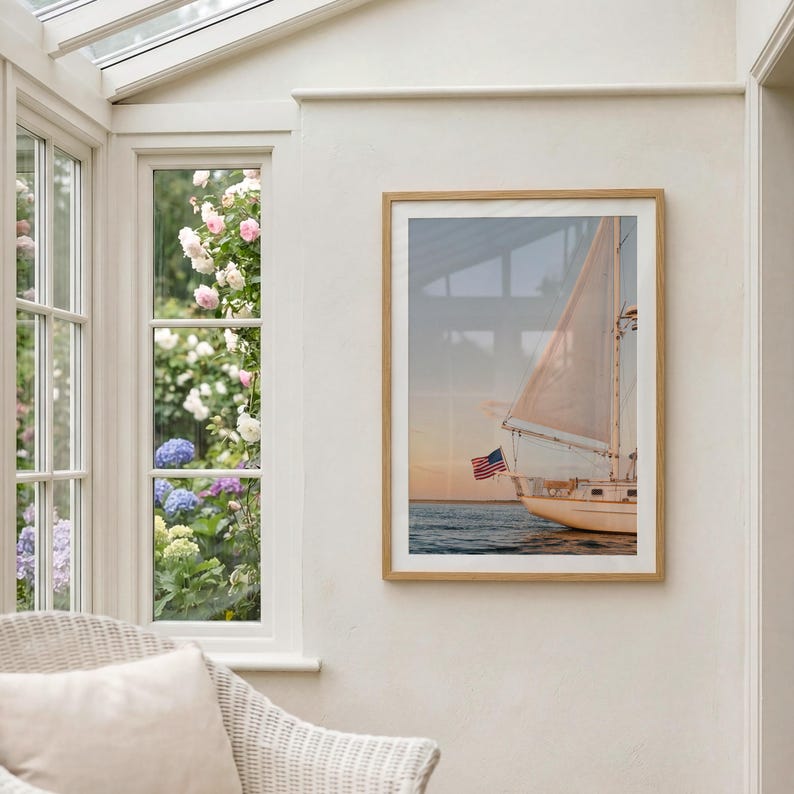 K&ouml;nnte beinhalten: Gerahmtes Foto eines Segelbootes auf dem Wasser mit amerikanischer Flagge. Das Segelboot hat einen wei&szlig;en Rumpf und Segel, mit Sonnenuntergang im Hintergrund. Das Foto ist in einem hellen Holzrahmen.