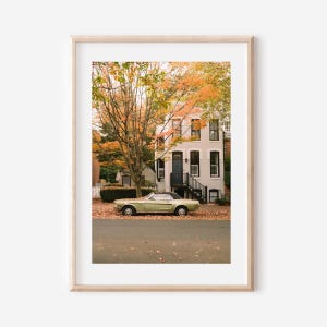Peut inclure: Impression encadrée d'une voiture décapotable vintage garée devant un immeuble. La voiture est vert clair avec un toit noir. La scène se déroule en automne, avec des feuilles orange et jaunes sur les arbres.