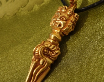 Può includere: Una collana con un ciondolo dorato con un designo dettagliato e ornato. Il ciondolo presenta un viso stilizzato con una forma appuntita, simile a un pugnale.