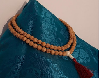 May include: A double strand of brown wooden beads with a white bead and a red tassel. The beads are on a teal blue fabric with a floral pattern.