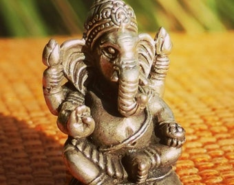 May include: A silver figurine of Ganesha, the Hindu god of wisdom and prosperity, with a trunk, large ears, and a crown. The figurine is sitting on a base with a decorative design.