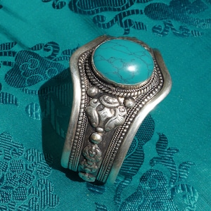 May include: A silver bracelet featuring a large turquoise stone set in the centre. The bracelet is adorned with intricate silver designs.