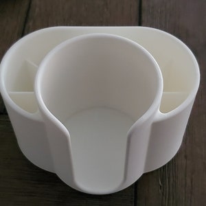 May include: White plastic desk organizer with a cup holder and compartments for pens and pencils.